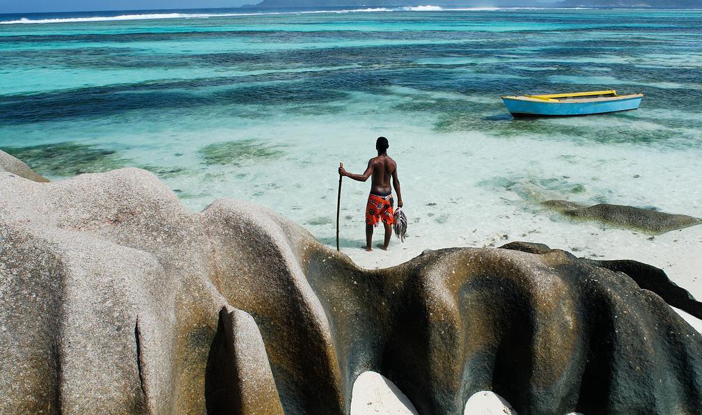 Homme sur une plage avec rochers et barque, Seychelles. - Aventure pirate aux Seychelles - 7