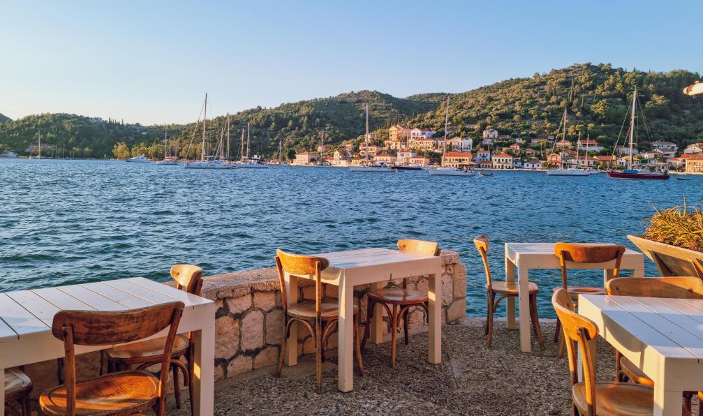Aleksandar - Adobestock - Tables de restaurant surplombant la baie de Vathy, à Ithaque, au coucher du soleil, avec en arrière-plan les maisons traditionnelles et colorées de larchitecture ionienne, Ithaque, Grèce. - Voile et rando en mer Ionienne  - 4