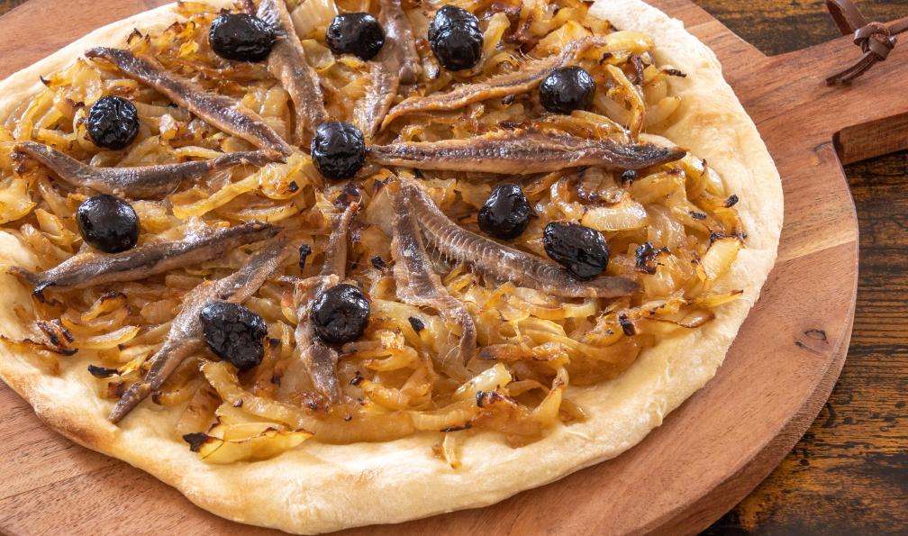 ALF photo - Adobe Stock - Pissaladière avec oignons, anchois et olives cuite sur une planche en bois, France - Calanques de Cassis et Côte Bleue - 13