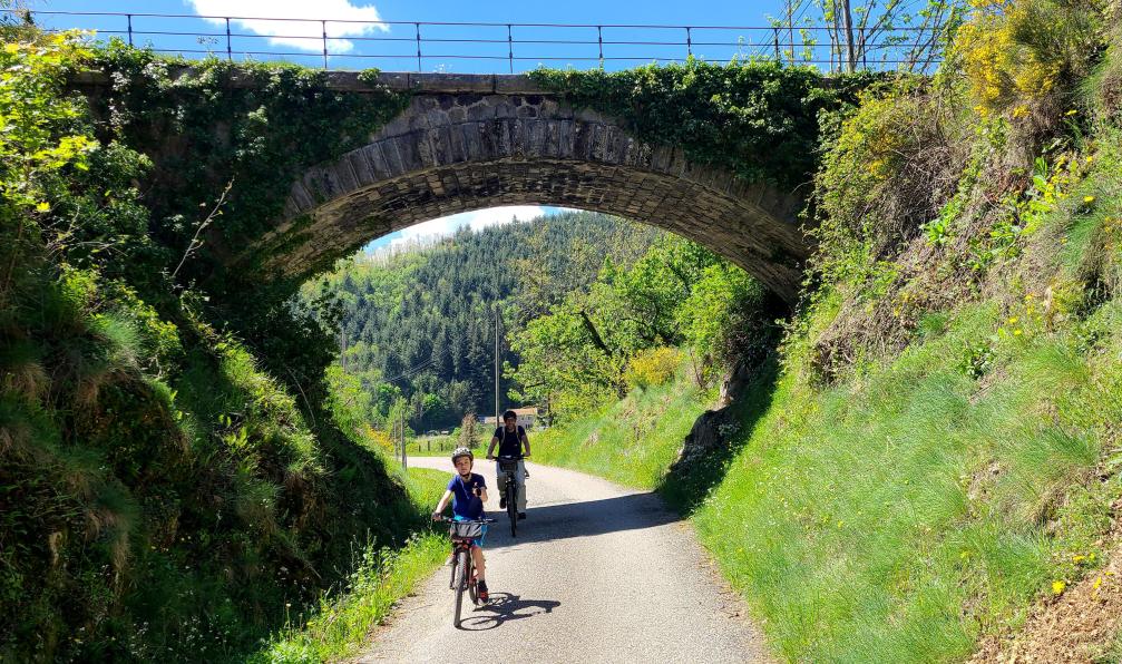 Aurélie Mansiot - Enfants à vélo, sur un chemin sous un pont en pierre, durant un voyage en famille sur la via dolce, Massif central, Ardèche, France - La Dolce Via à vélo en famille - 3