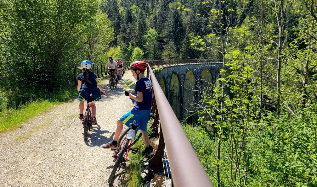 Aurélie Mansiot - Enfants à vélo, contre une barrière sur un pont en pierre avant une forêt, durant un voyage en famille sur la via dolce, Massif central, Ardèche, France - La Dolce Via à vélo en famille - 6
