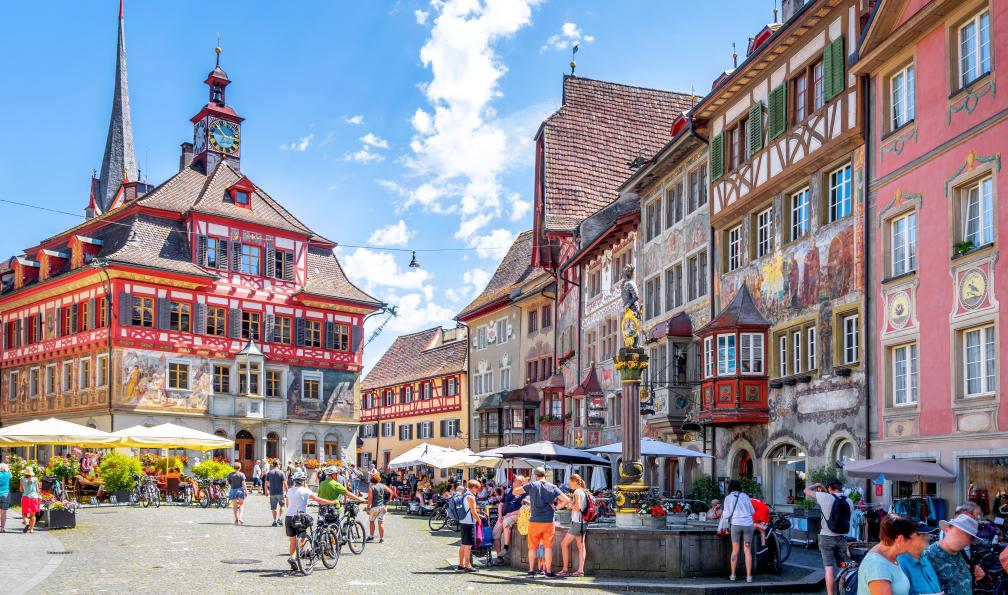 Ettmer - Sina - Adobe Stock - Hôtel de ville et placette avec cyclistes à Stein am Rhein (Suisse) - Le tour du lac de Constance sportif à vélo - 4