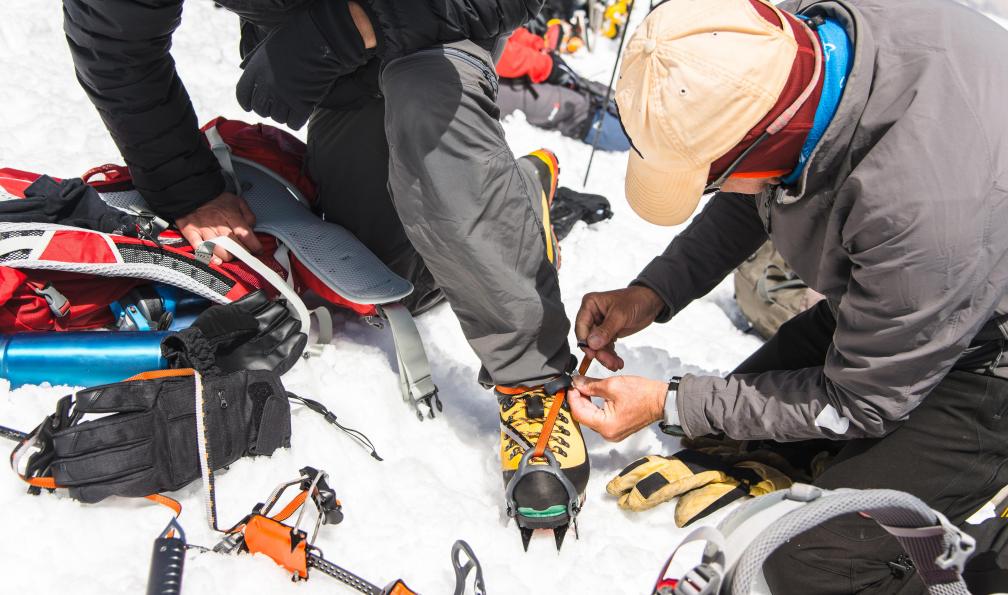 yanik88 - Istock - Guide aidant un alpiniste à chausser ses crampons;France - Préparation aux trekking peaks et expéditions - 1