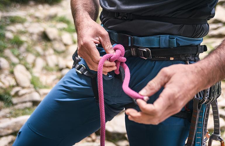 Cadrage sur un homme réalisant un noeud pour escalader une paroi
